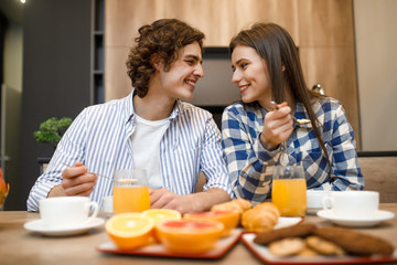 Married lovely couple in love eating breakfast together in morning at kitchen, happy family, romantic, healthy food, cornflakes with milk, orange and croissant at the table