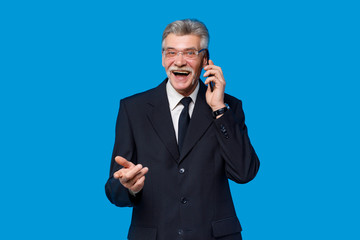 People lifestyle concept. Holding mobile phone elderly gray-haired mustache bearded man in classic suit posing isolated on blue background in studio
