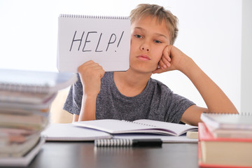 Upset tired preteen child sitting at the table, doing his homework among pile of books. Word Help...