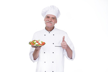 Cooking and professional culinary concept, elderly professional chef in white uniform holds vegetable salad stay isolated white background