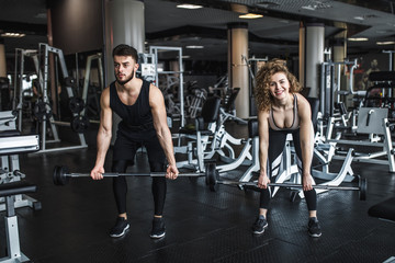 Fototapeta na wymiar Fitness and young couple exercising in gym with barbell weights