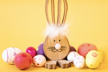 Wooden Easter Bunny with Easter eggs, on an isolated yellow background