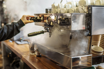 Coffee machine in steam, barista preparing coffee at modern cafe