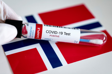 Testing for presence of coronavirus in Norway. Tube containing a swab sample that has tested positive for COVID-19. Norwegian flag in the background.