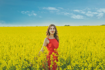 Fototapeta premium Young beautiful girl in a red dress close up in the middle of the yellow field with the radish flowers