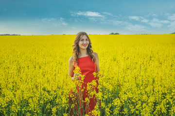 Naklejka na ściany i meble Young beautiful girl in a red dress close up in the middle of the yellow field with the radish flowers