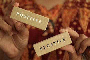 Young woman holding antonym word sign of positive and negative. Two wooden blocks in hands with...