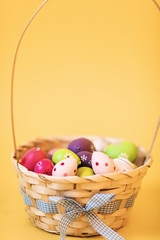 Colorful Easter eggs in a basket on an isolated yellow background