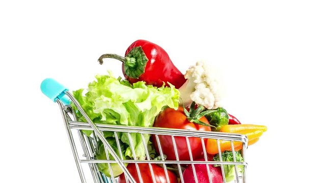 Shopping cart moving fast from side to side and quickly filling with vegetables and fruits. Mountain of fresh vegetables and fruits in a overcrowded trolley. Consumerism, sale and shopping concept.