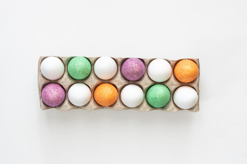 Fototapeta na wymiar Dozen coloured and white easter eggs in a carton on white background