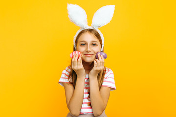 Beautiful happy girl on her head with rabbit ears and colorful Easter eggs in her hands, on a yellow background