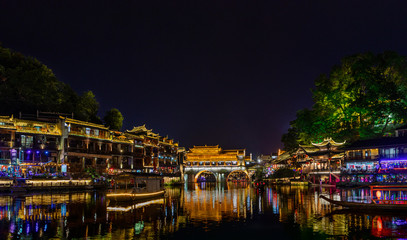 Night view of Hong Bridge & stilt houses of Tujia Minority by riversides of Tuo River in Fenghuang Ancient Town built in 1704 in western Hunan, China. UNESCO World Heritage.