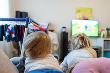 Back view of two cute little caucasian little boy and girl lying on sofa watching cartoons or movie on tv set with streaming service. Children stay home quarantine coronavirus outbreak spread danger