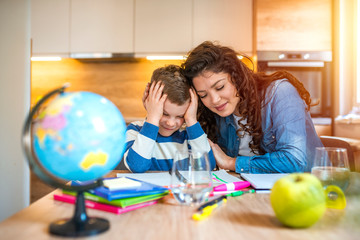 Young mother sitting at a table at home helping her small son with his homework from school. A mother at a table at home helping her small son with his homework from school