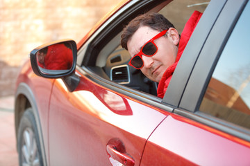 A young man driving a car wearing sunglasses smiles