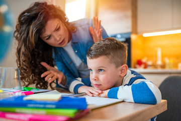 Obraz na płótnie Canvas Stressed mother and son frustrated over failure homework, school problems concept. Sad little boy turned away from mother, does not want to do boring homework