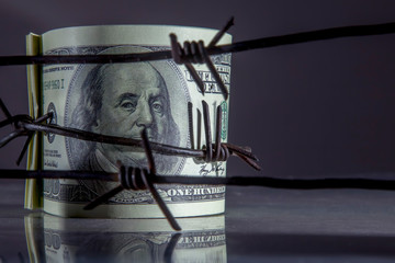 Economic warfare, sanctions and embargo busting concept. Close up US Dollar bills wrapped in barbed...