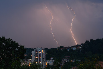 Lightning over the city at the summer storm. Dramatic, breathtaking atmospheric natural phenomenon.Beautiful dark storm sky. Clouds and thunder lightnings.Bright lightning in the black sky