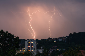 Lightning over the city at the summer storm. Dramatic, breathtaking atmospheric natural phenomenon.Beautiful dark storm sky. Clouds and thunder lightnings.Bright lightning in the black sky