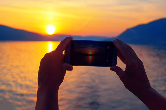 the smartphone in the hands takes the picture at sunset