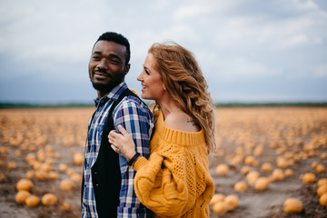 A young woman leaned against her husband's back while standing in a pumpkin field.