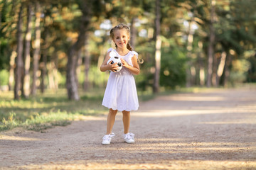 Portrait of a smiling little girl with a soccer ball in her hands. In the park on the road.