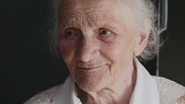 Portrait of cute, wrinkled grandmother looks at camera and talks on background