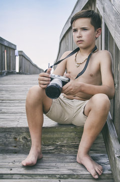 Young boy with camera sitting on boardwalk