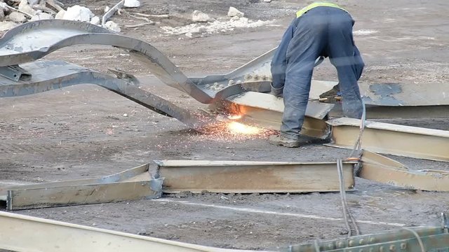 Welder flame cutting steel girders in slow motion