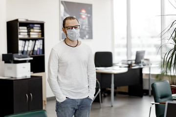 Man in a medical mask stands in front of an empty office.