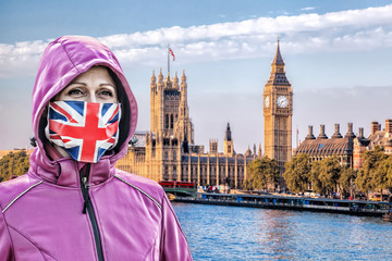 Woman wearing protection face mask with British flag against coronavirus in front the of Big Ben,...