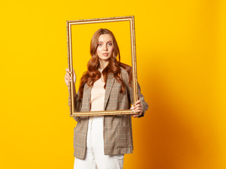 Fototapeta na wymiar portrait of woman with empty picture art frame isolated on yellow background