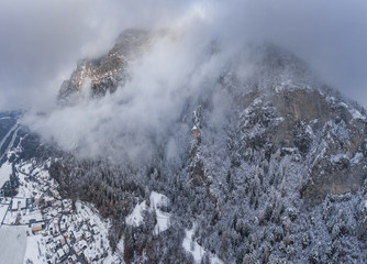 Aerial view of mountain with boundary tower, forest underneath fog, slopes with snow covered in Switzerland, cloudy atmosphere, beautiful conditions