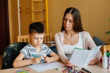 A young mother is doing homework with her son at home. Parents and training