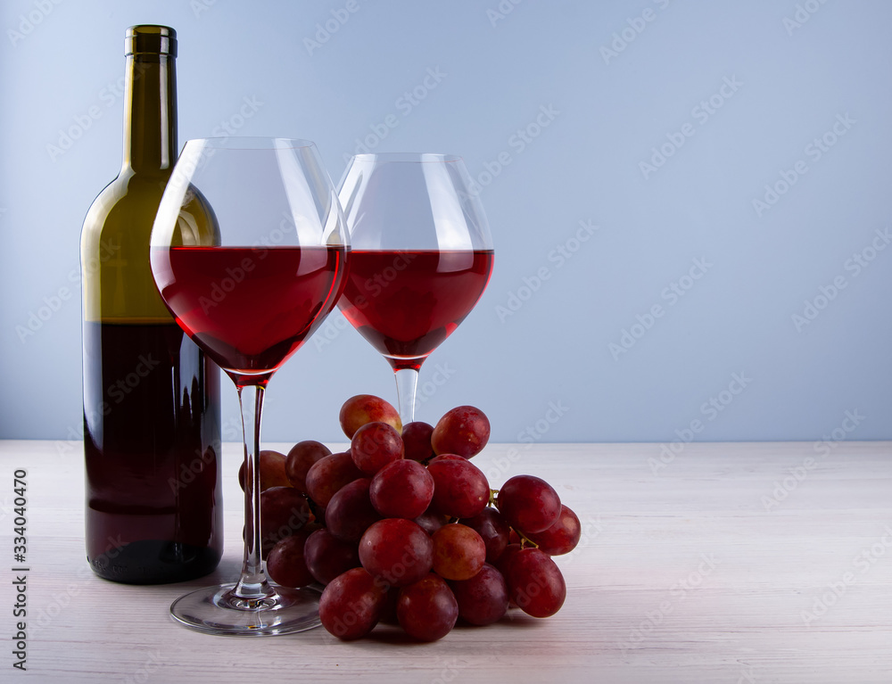 Wall mural low angle perspective with a two traditional glass filled with dark red wine and red grape and bootl