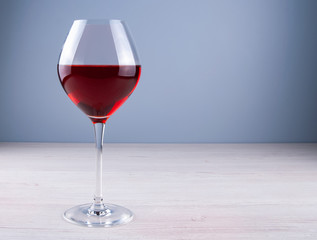 Low angle perspective of a crystal clear glass with a two traditional round glass filled with dark red wine and a thin leg on a wooden table with a light gray background with copy space for your text