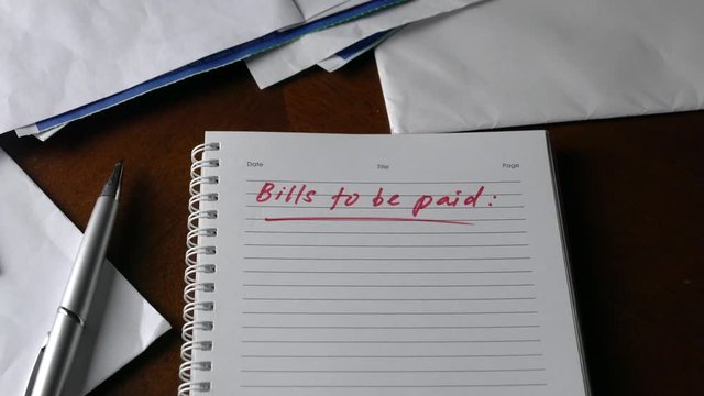 Bills to be paid, red color words written on notepad with bills and invoices at the background. Economy recession and unemployment concept.