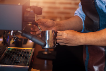 Barista steaming milk in the pitcher with coffee machine for  preparing to make latte art.