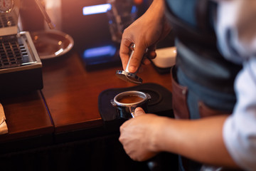 Barista holding portafilter and coffee tamper making  coffee at cafe.