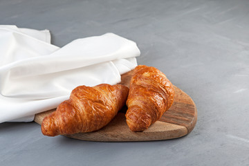 Two fresh croissants lie on a wooden cutting board next to a white napkin. Close-up, place for text
