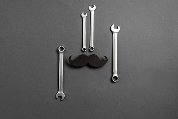 Creative flat lay overhead top view retro stylish black funny paper moustache and combination wrenches on grey background with copy space. Men health awareness month fathers day masculinity concept
