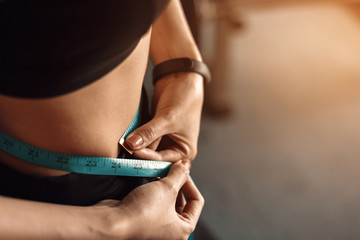Athletic slim woman measuring her waist by measure tape after workout and exercise in gym.