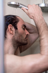 Handsome young single male washing his body and face in bathroom.