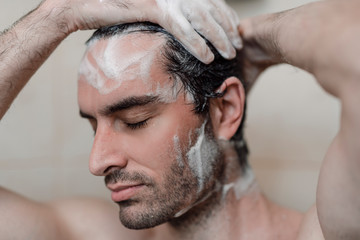 Handsome young single male washing his body and face in bathroom.