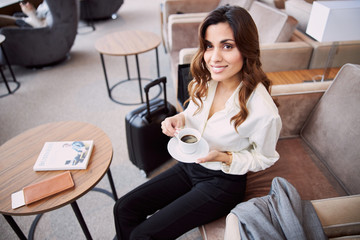 Charming lady drinking coffee in airport departure lounge