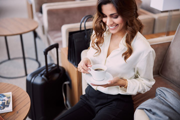 Joyful lady drinking coffee in airport departure lounge