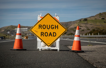 Yellow traffic control sign stating Rough Road on highway shot in late afternoon sun. A car is...