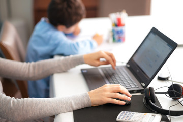 mother at home, smart working with laptop and headphones, while child is drawing