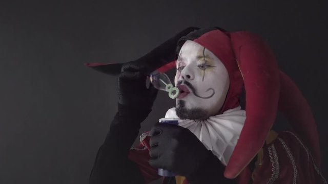 Street artist in a costume of Jester making bubbles, circus performance of a happy harlequin. Slow motion	