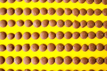 Drops of milk chocolate are laid out in a row on a yellow background